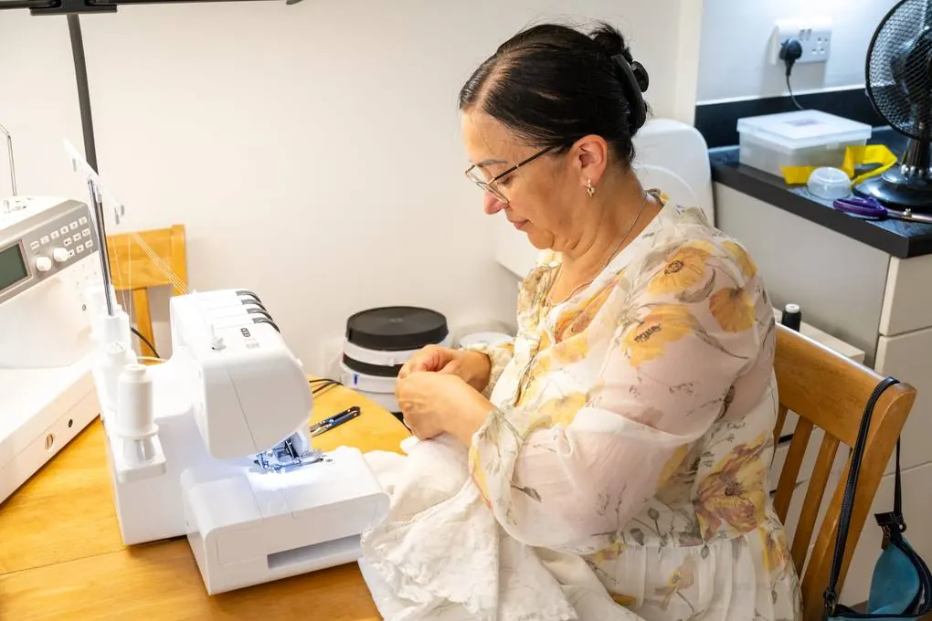 Afina working at the overlocker on a length of pale fabric