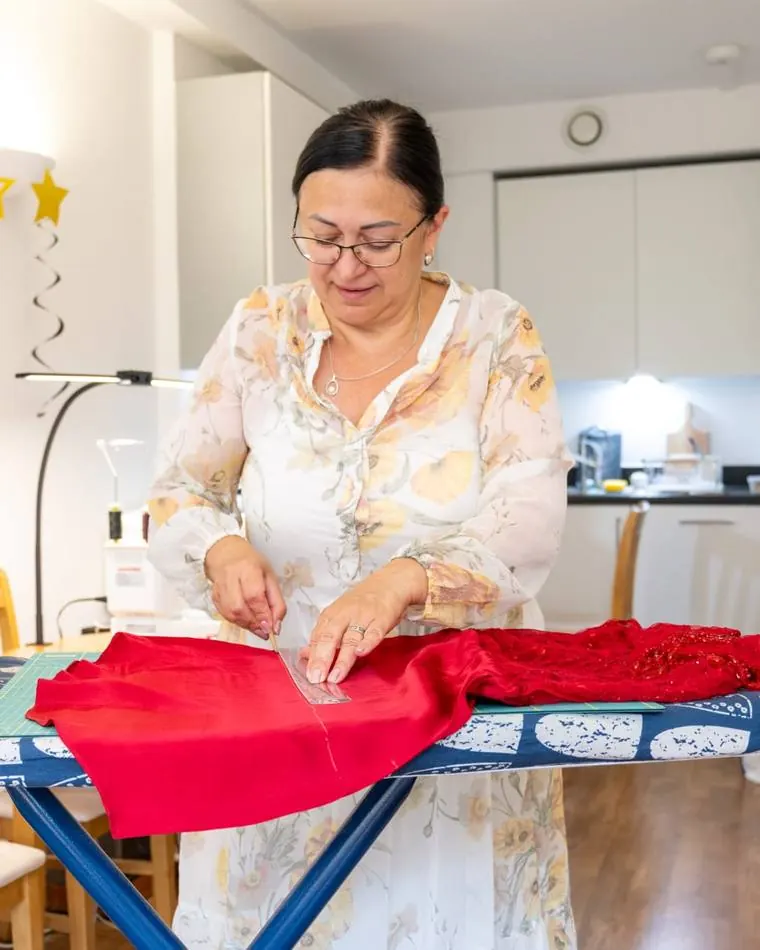 Afina measuring and marking a red garment on the pressing board in her Brighton studio